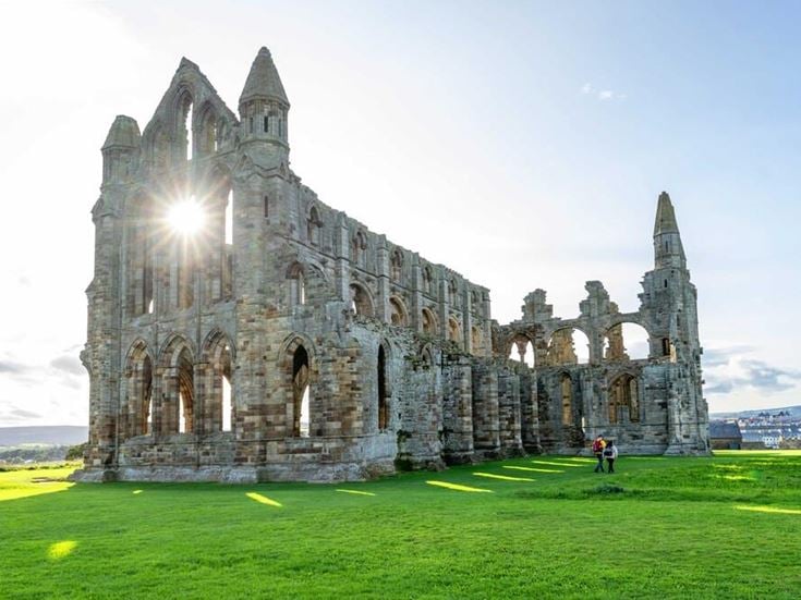 a large stone building with a grass field in front of it with Whitby Abbey in the background